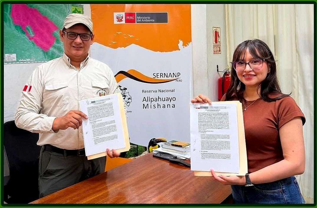 Dos personas muestran el contrato firmado frente a un banner del SERNANP y de la Reserva Nacional Allpahuayo Mishana